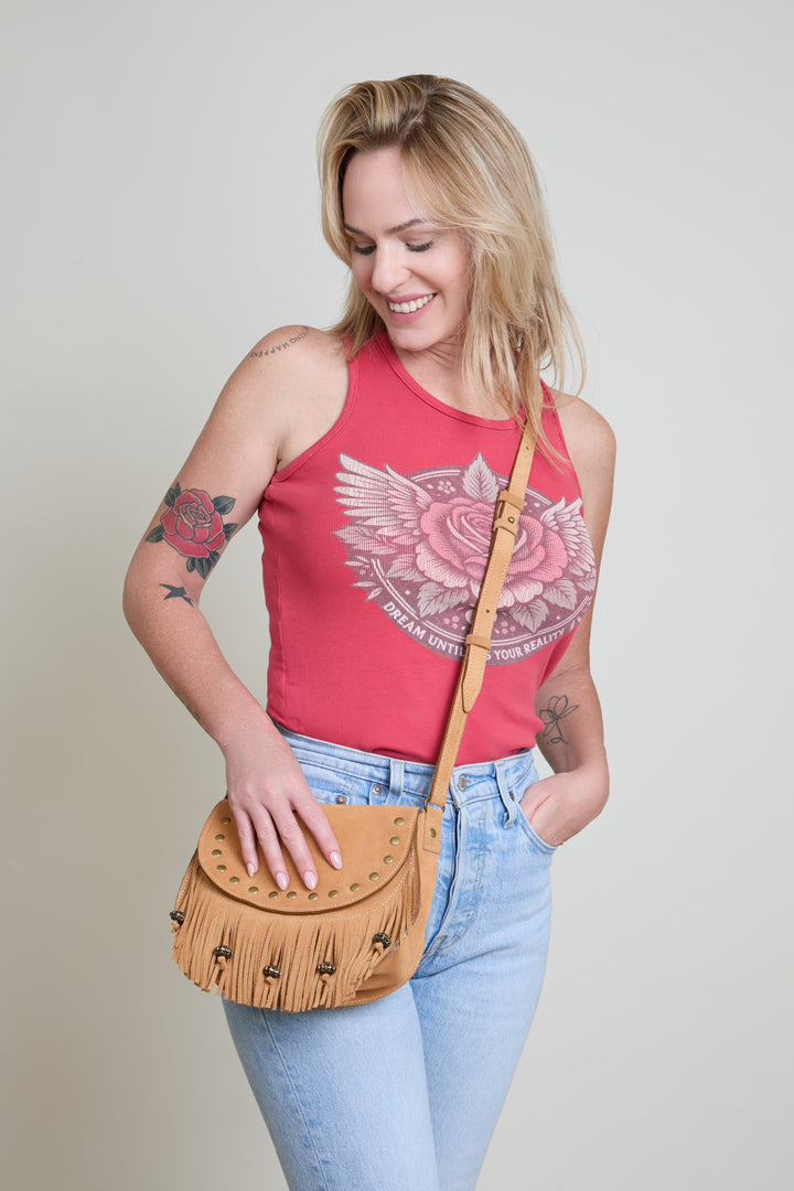 Woman wearing a red tank top with a floral design and holding a tan fringed handbag against a plain background