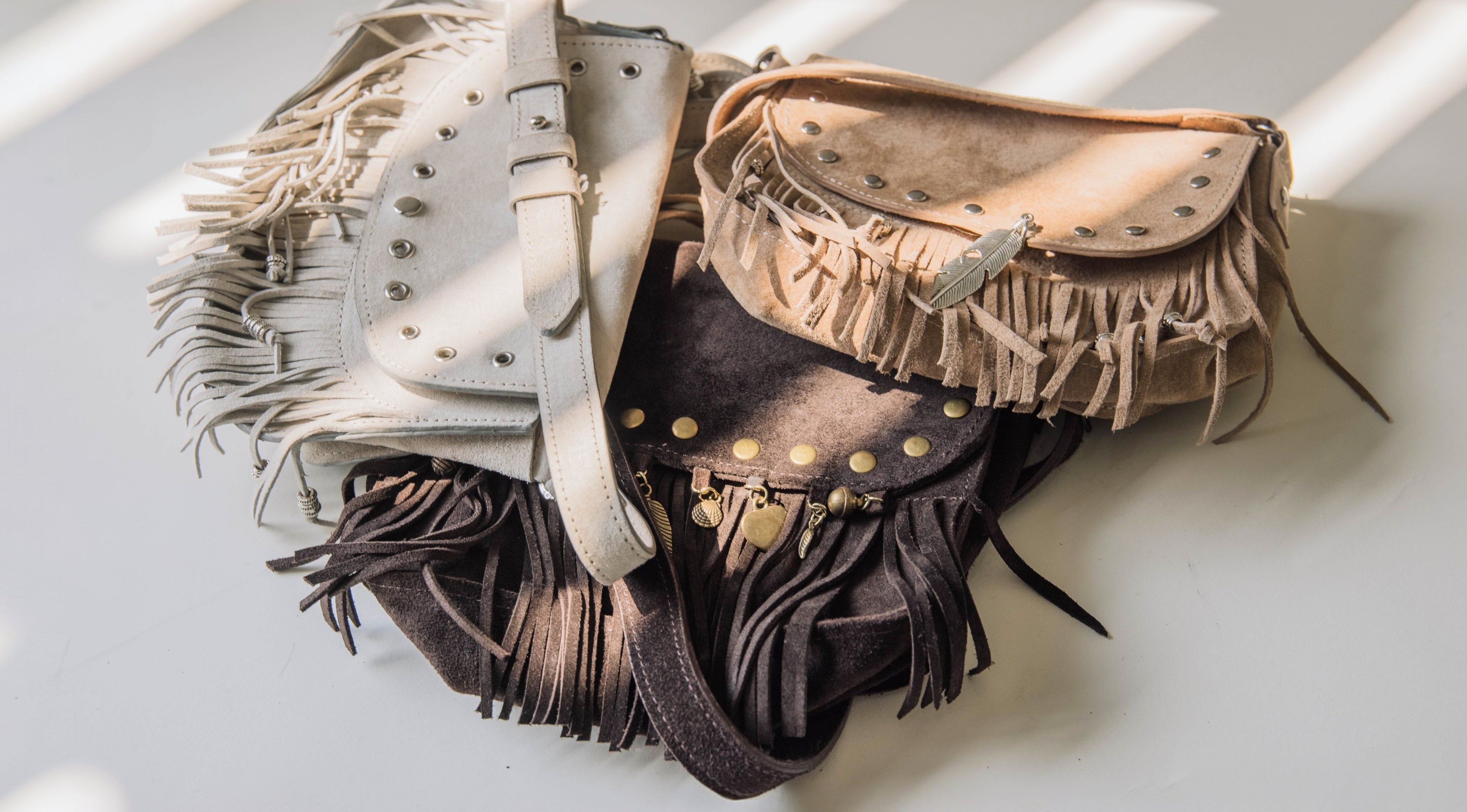 Three leather bags with fringe and studs on a light background