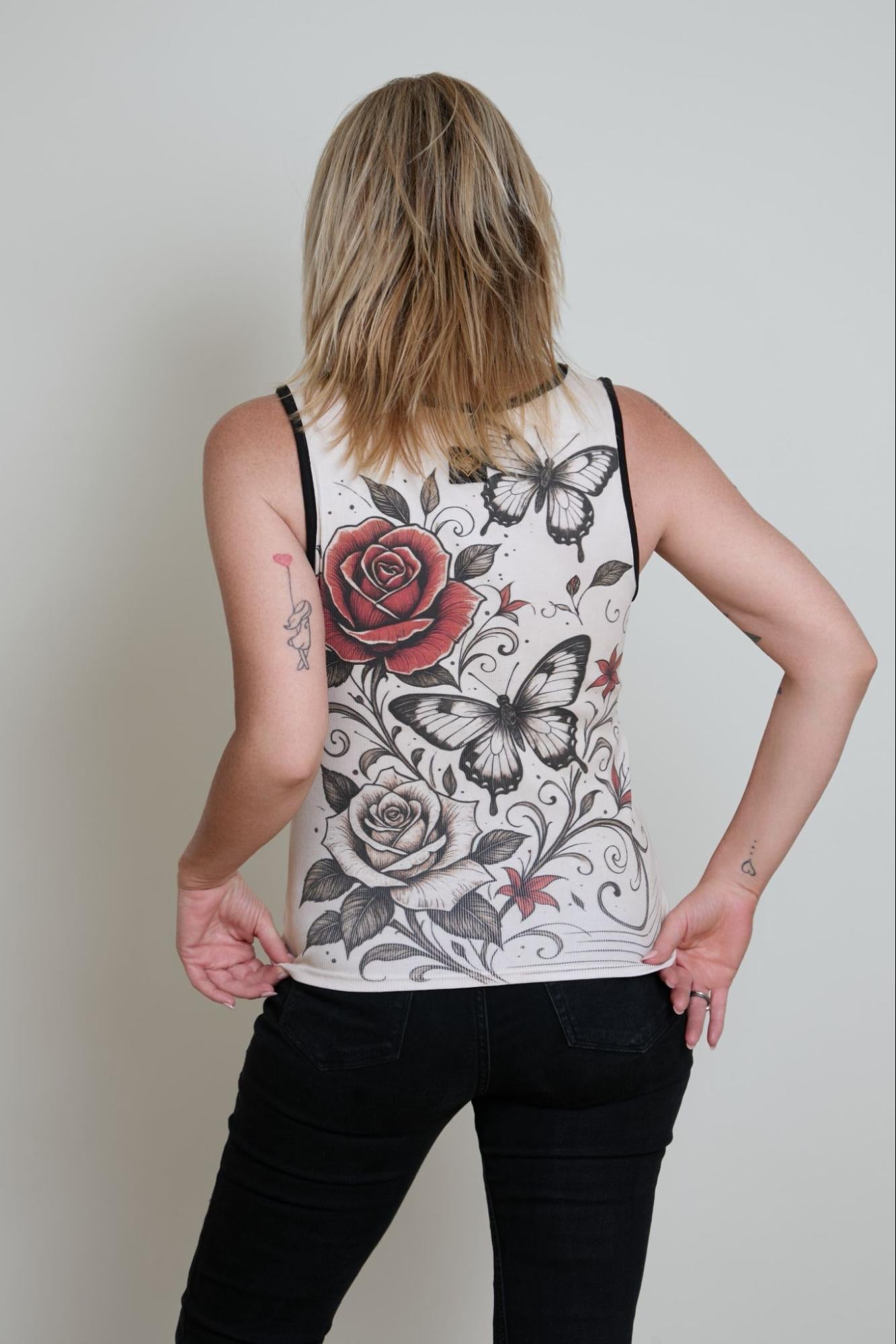 Person wearing a tank top with floral and butterfly designs on a plain background
