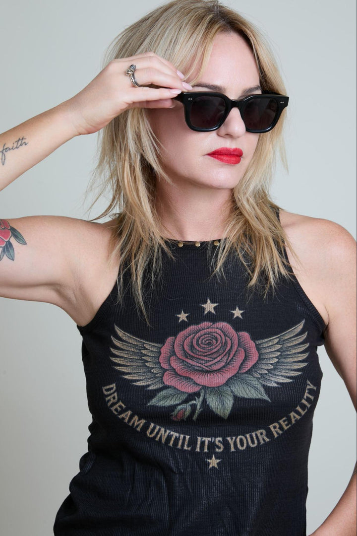 Woman wearing a black tank top with a rose design and text, holding sunglasses.