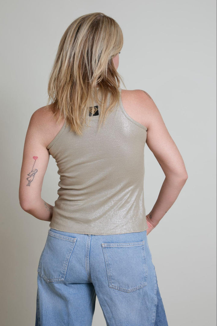 Person wearing a beige tank top and blue jeans against a plain background