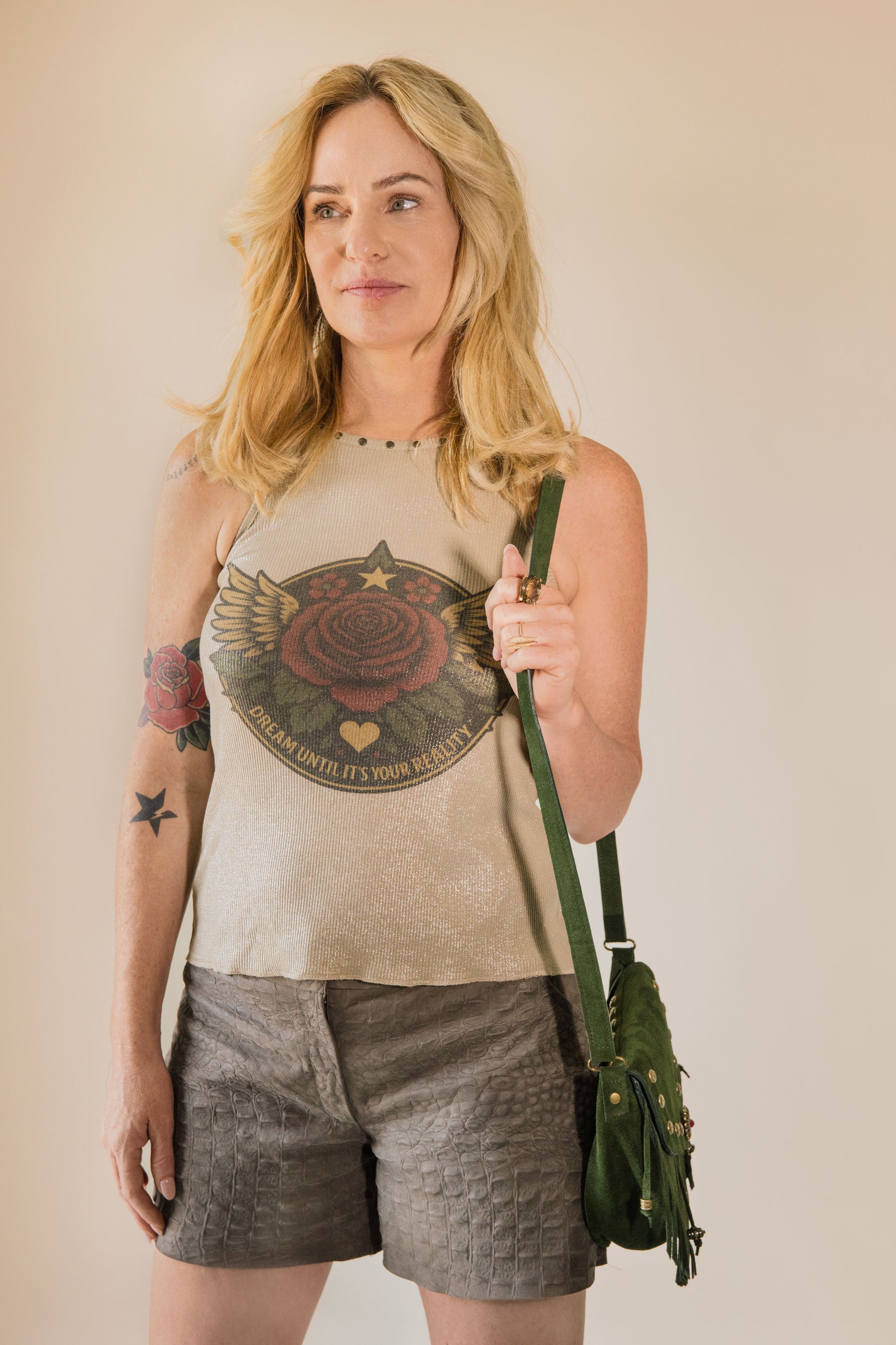 Woman wearing a tank top with a graphic design, holding a green bag against a plain background
