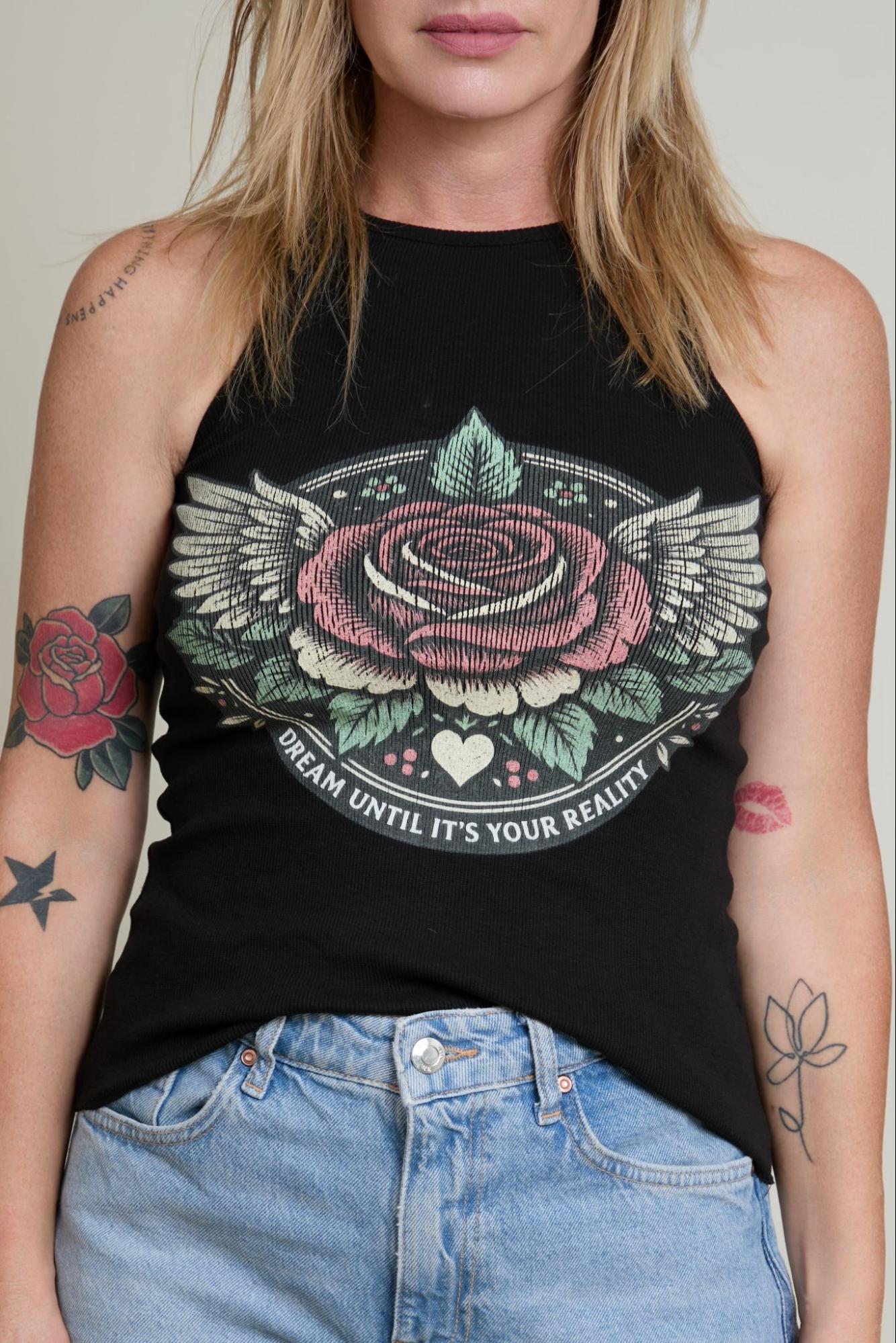 Person wearing a black tank top with a rose and wings design, standing against a neutral background.