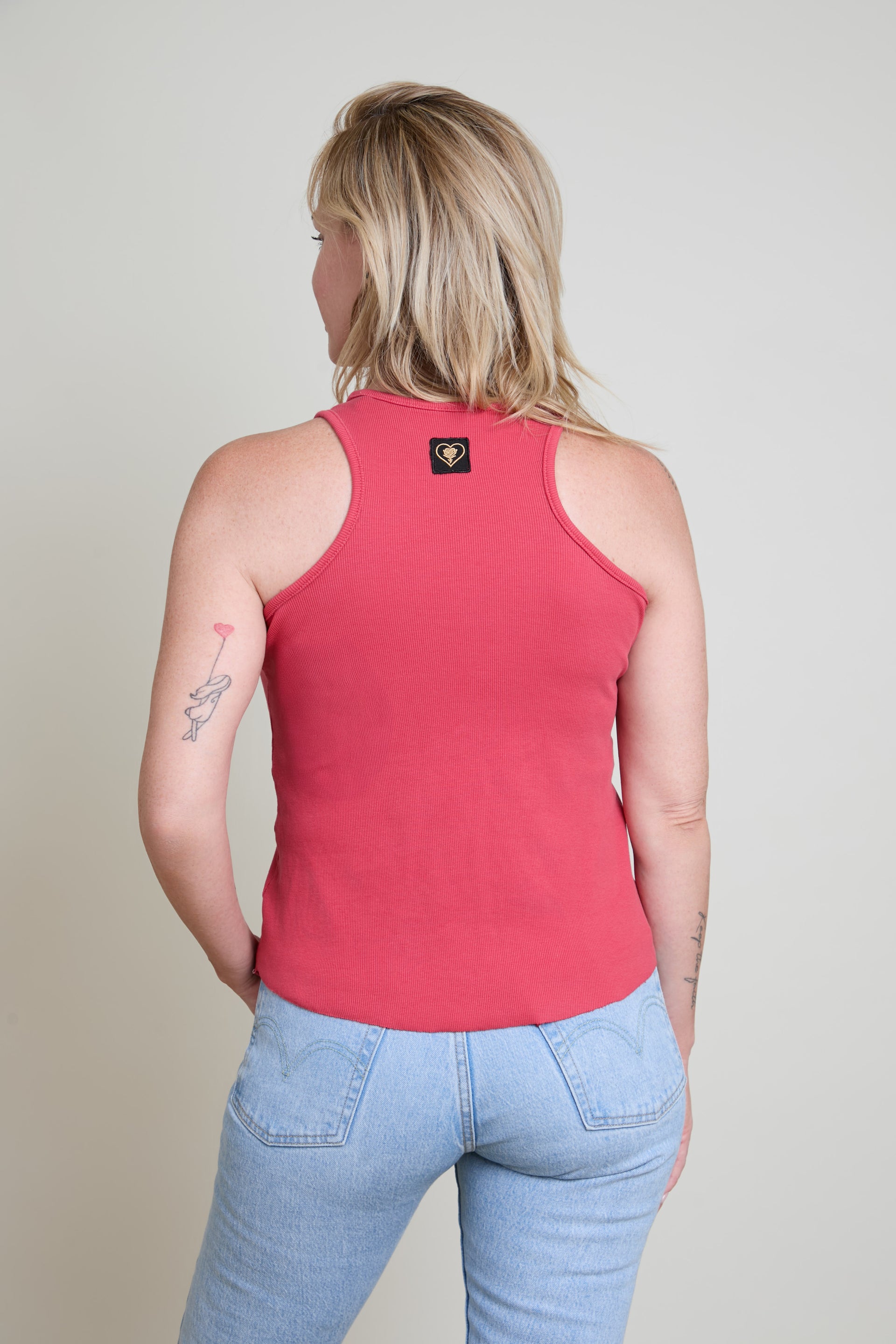 Person wearing a red tank top and light blue jeans on a plain background