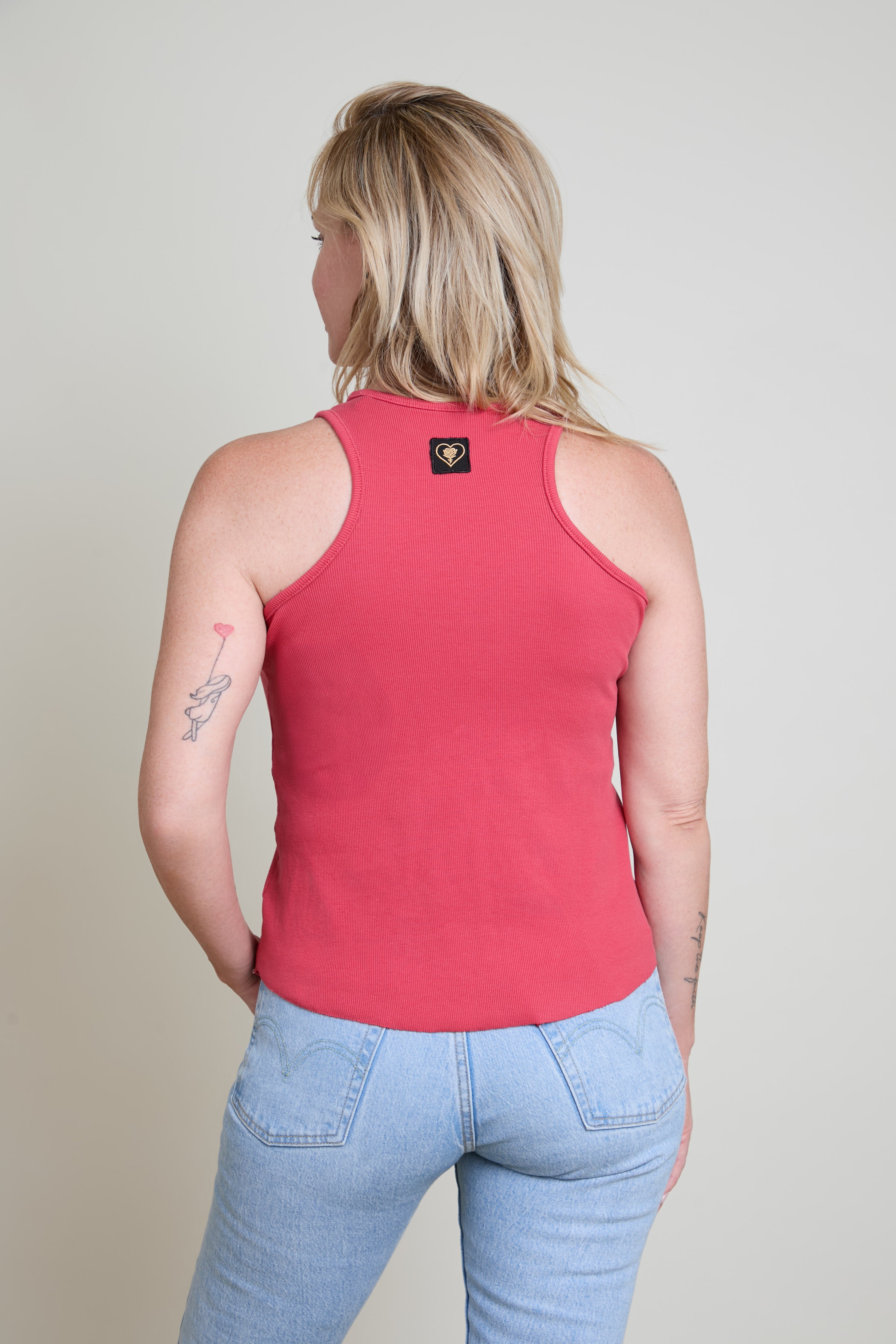 Person wearing a red tank top and light blue jeans on a plain background