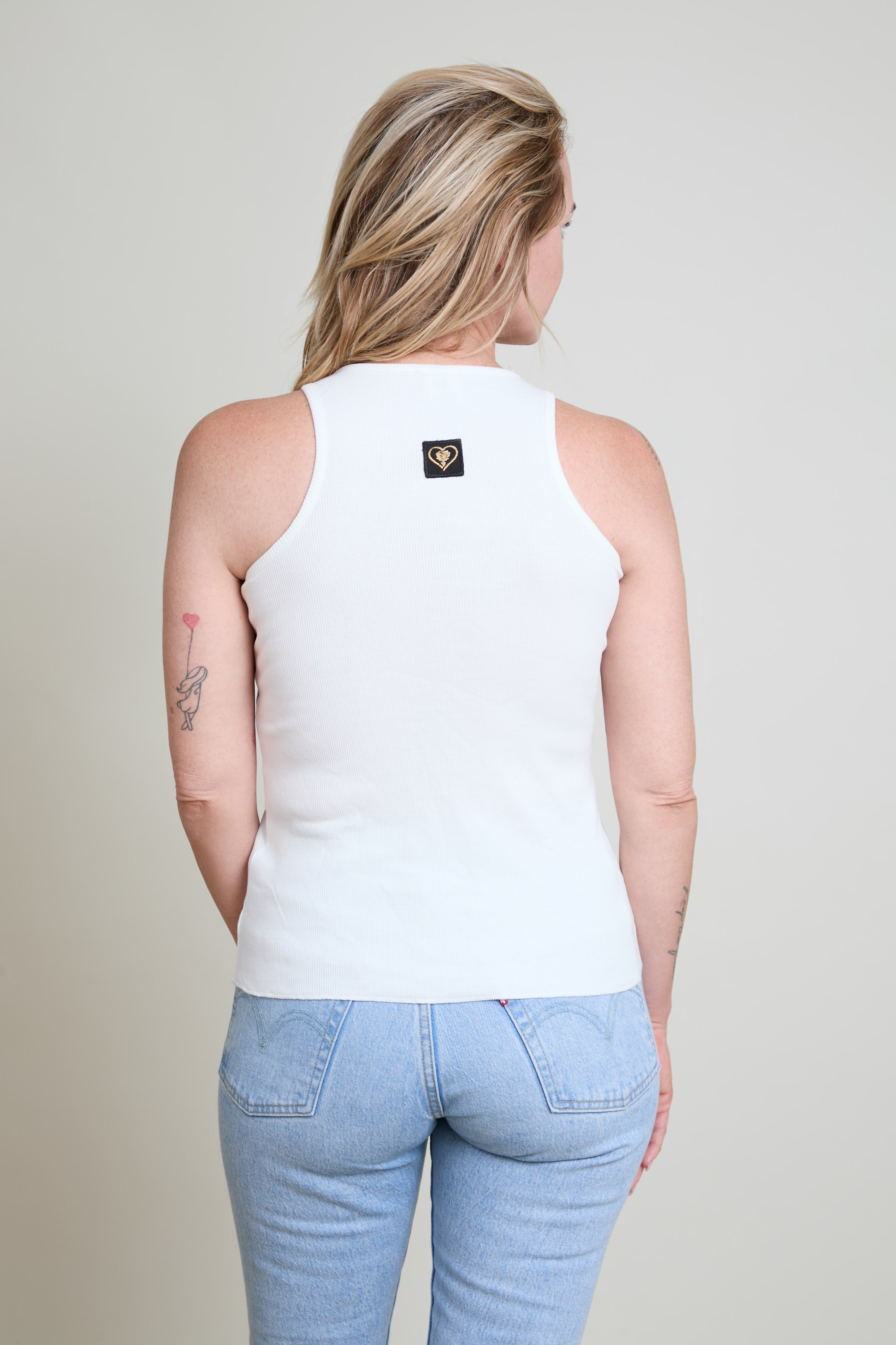 Person wearing a white sleeveless top with a logo on a plain background