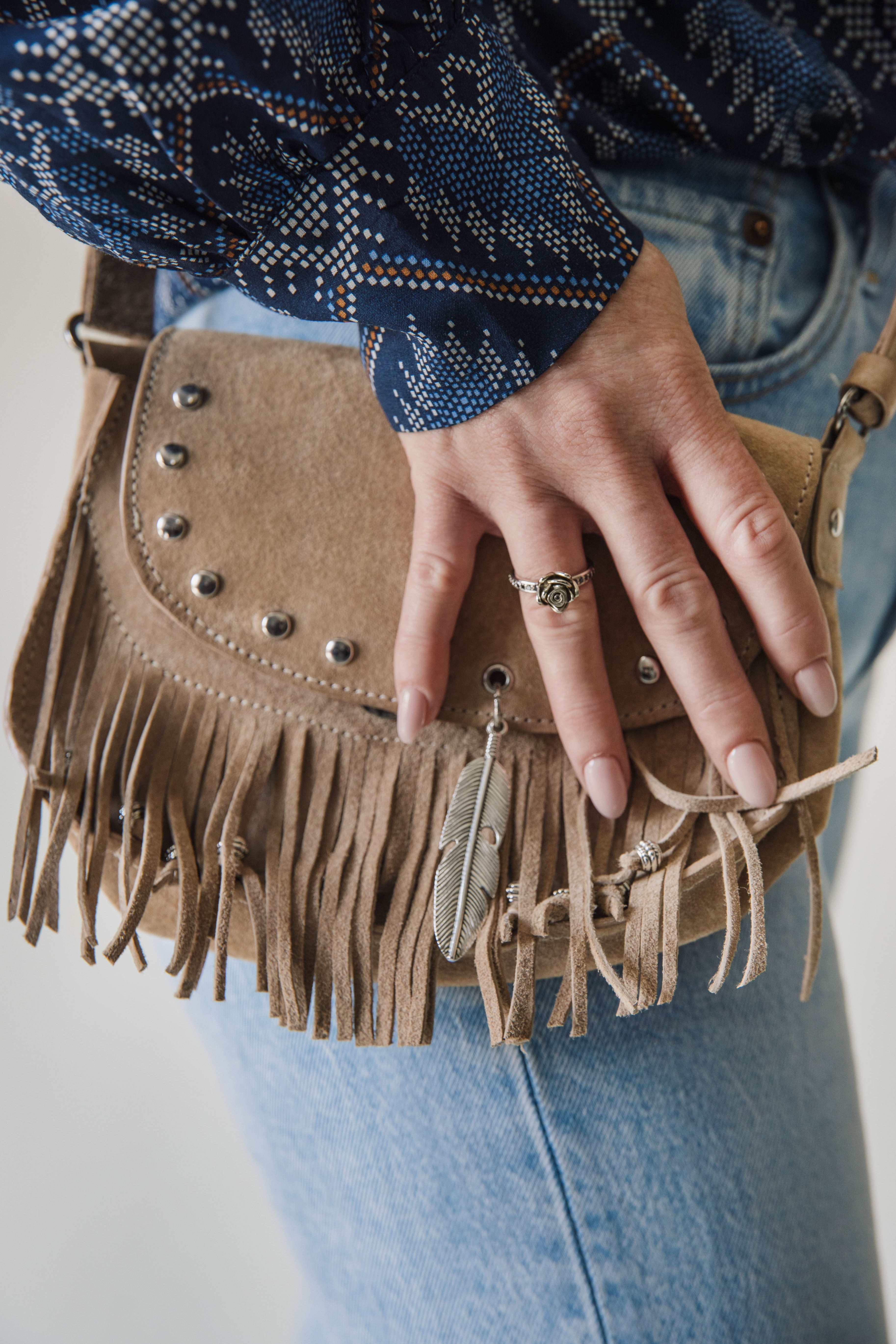 Person holding a brown suede handbag with fringe details