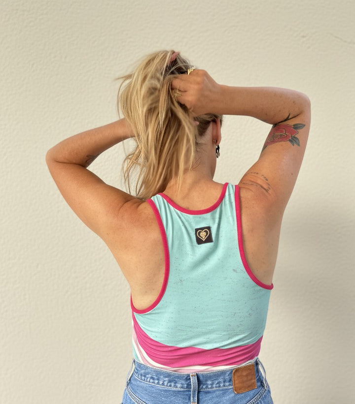 Person wearing a light blue and pink tank top with a visible brand logo, standing against a plain background.