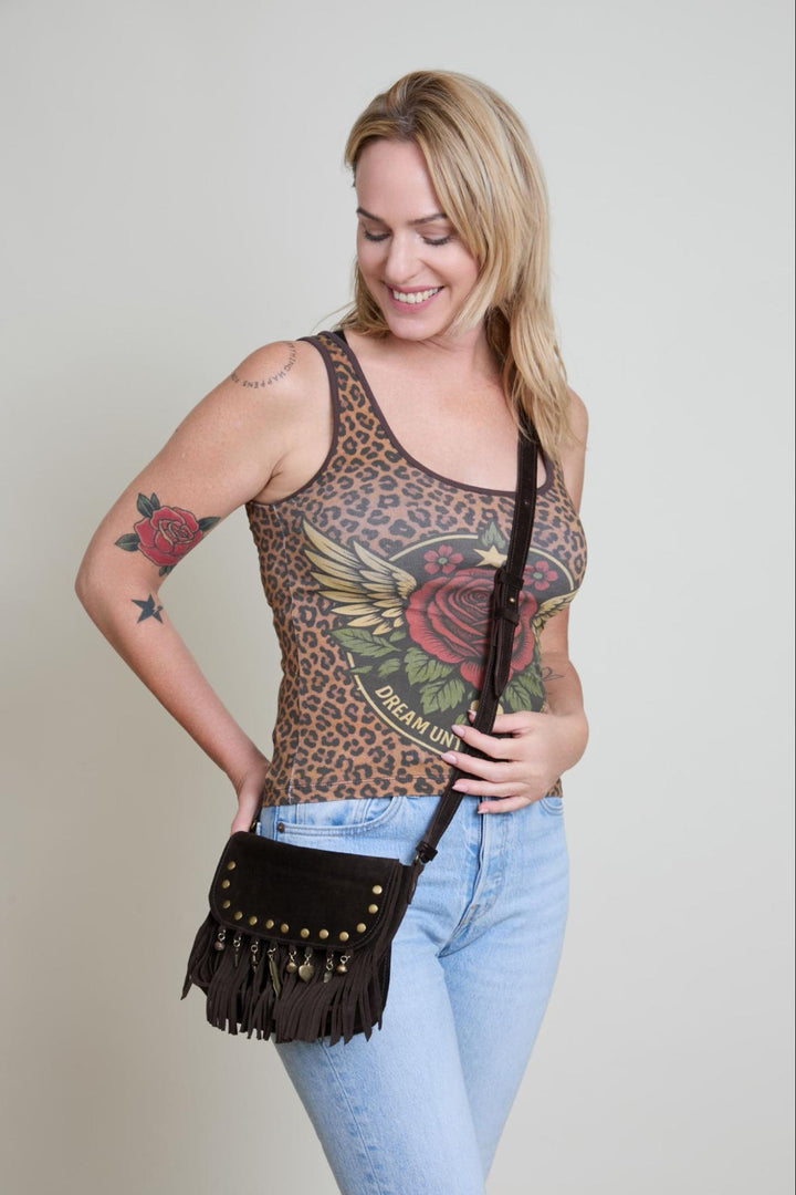 Woman wearing a leopard print tank top with floral designs, holding a black fringe bag against a plain background.