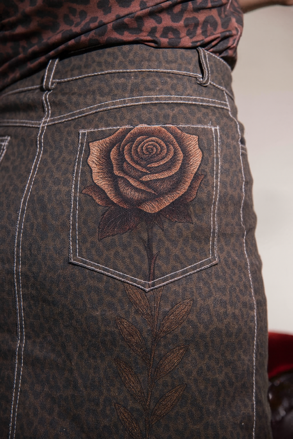 Close-up of a brown denim pocket with a rose design on a patterned shirt background