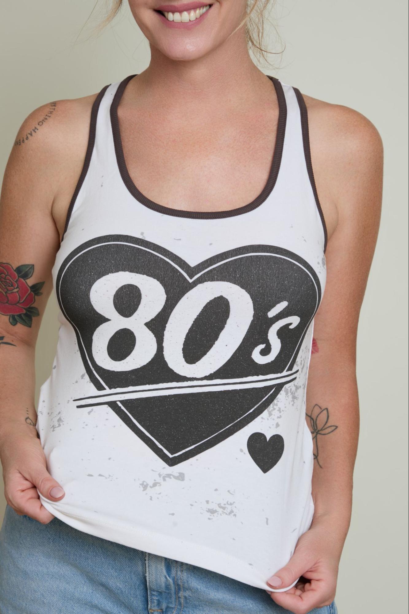 Person wearing a white tank top with '80s' design on a plain background