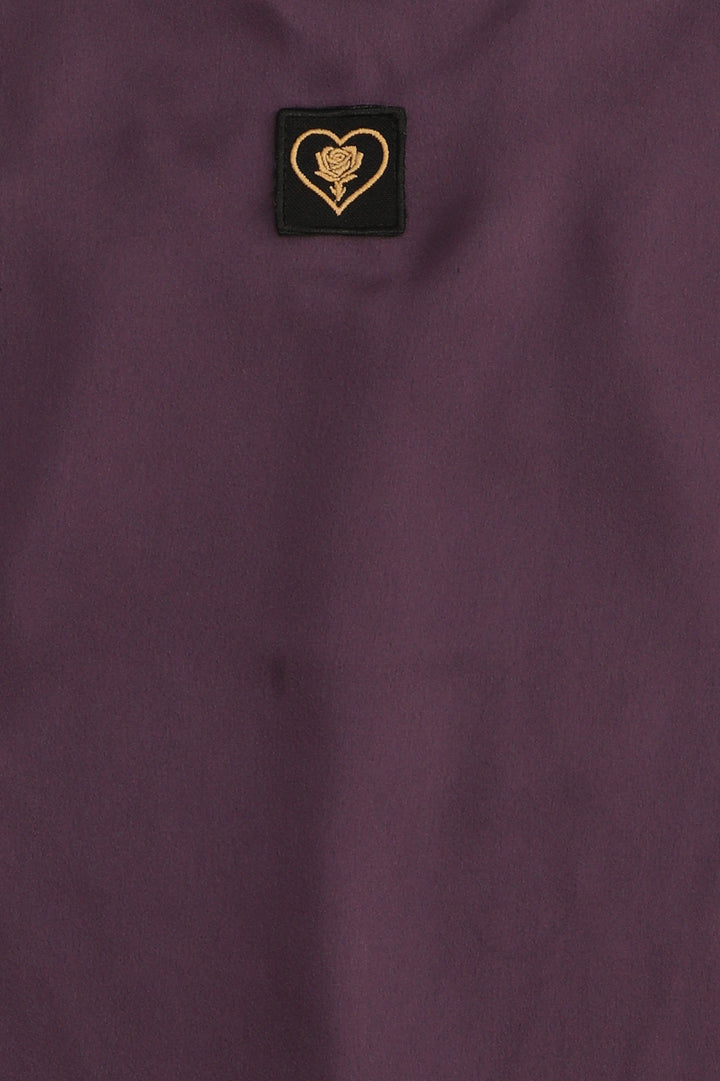 Close-up of a purple fabric with a small embroidered heart and rose design on a black background.