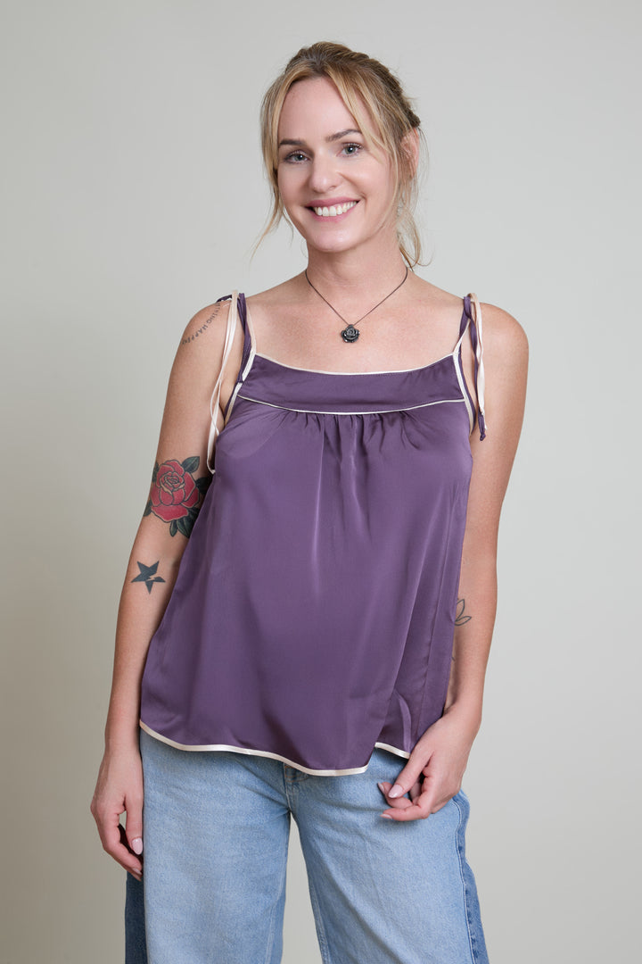 Woman wearing a purple tank top and blue jeans against a plain background