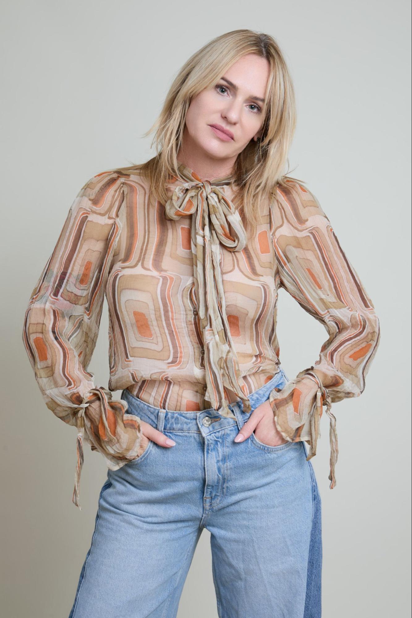 Woman wearing a patterned blouse and blue jeans against a plain background