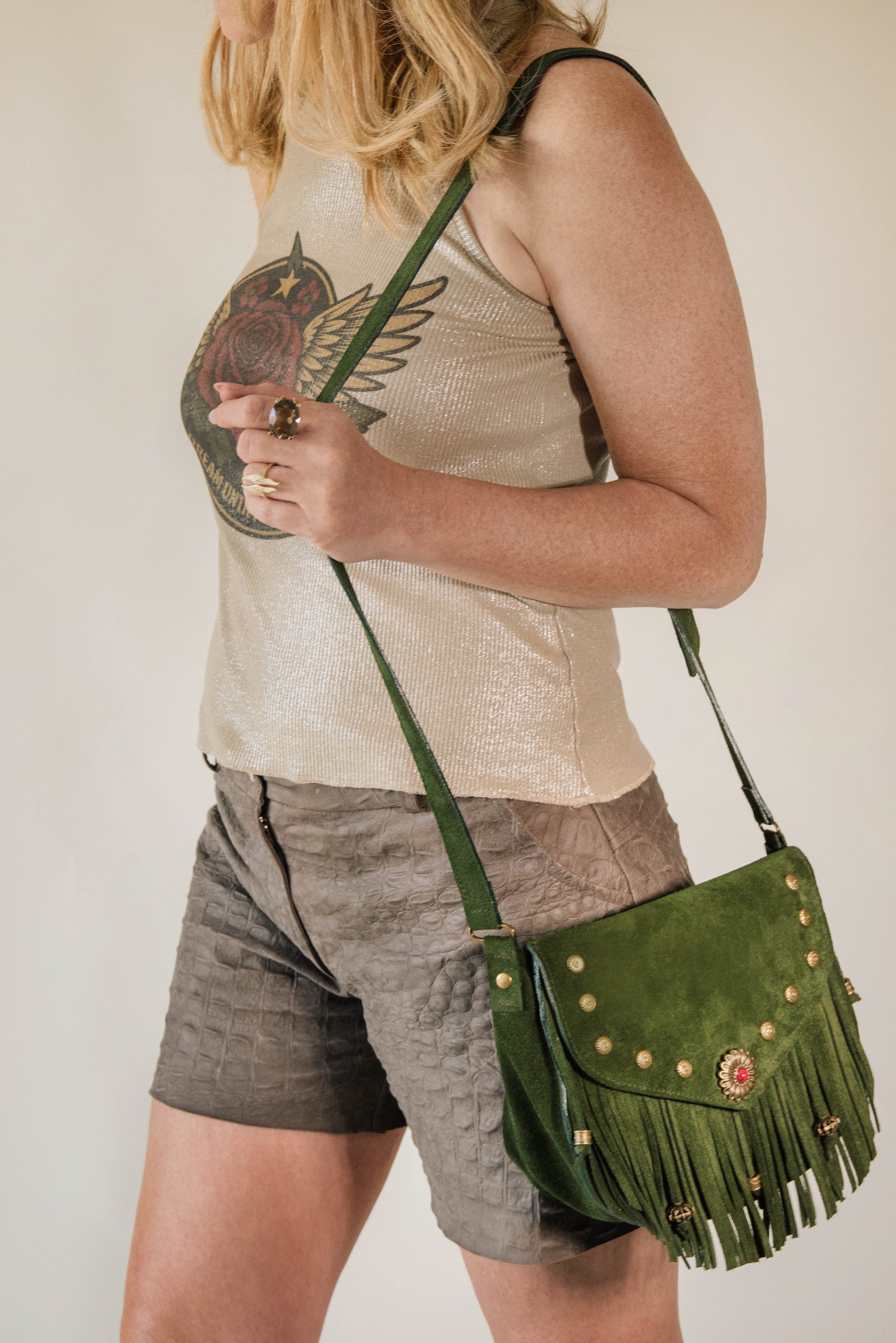Person wearing a beige tank top and gray shorts with a green fringed handbag.