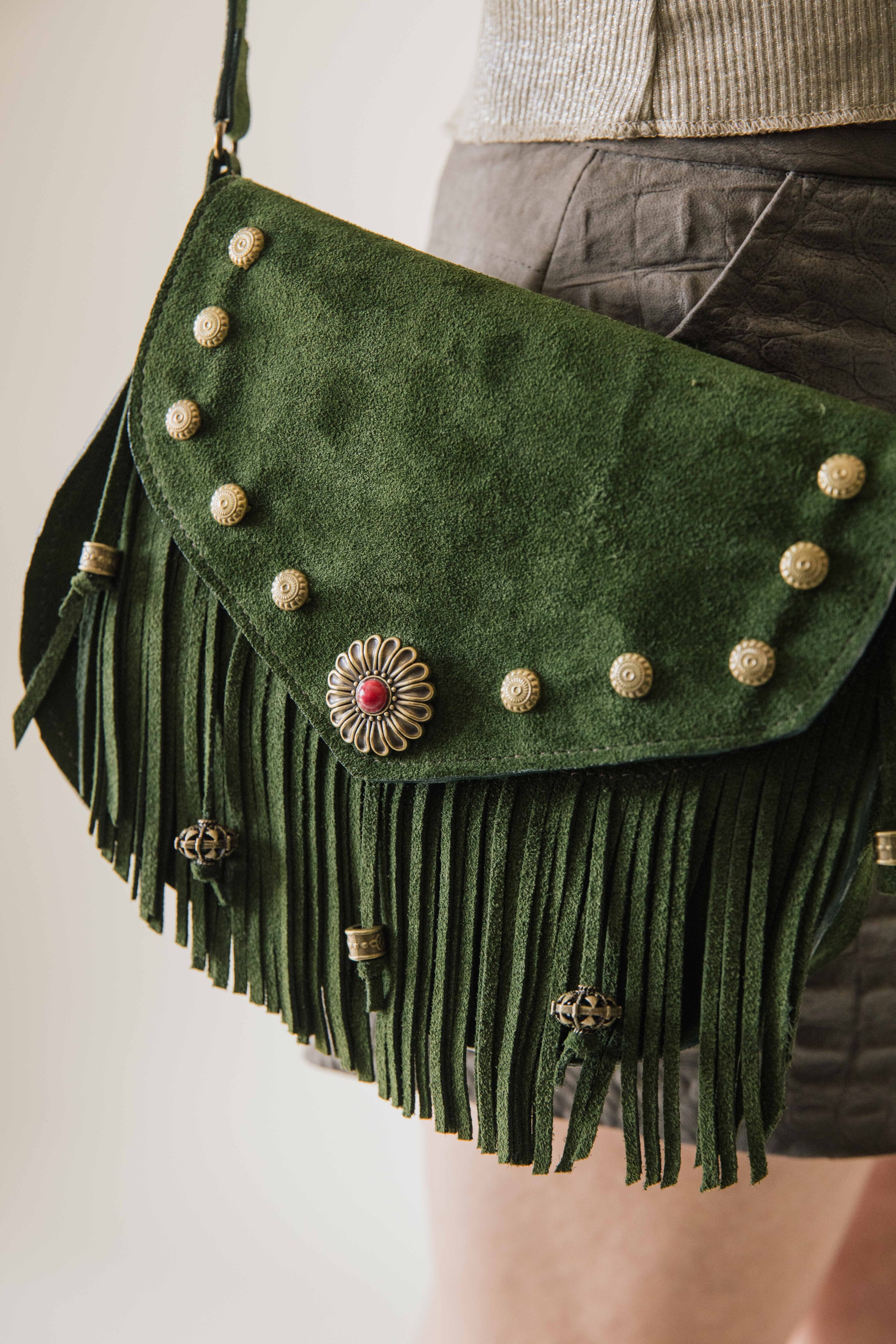 Green suede handbag with fringes and decorative buttons on a plain background