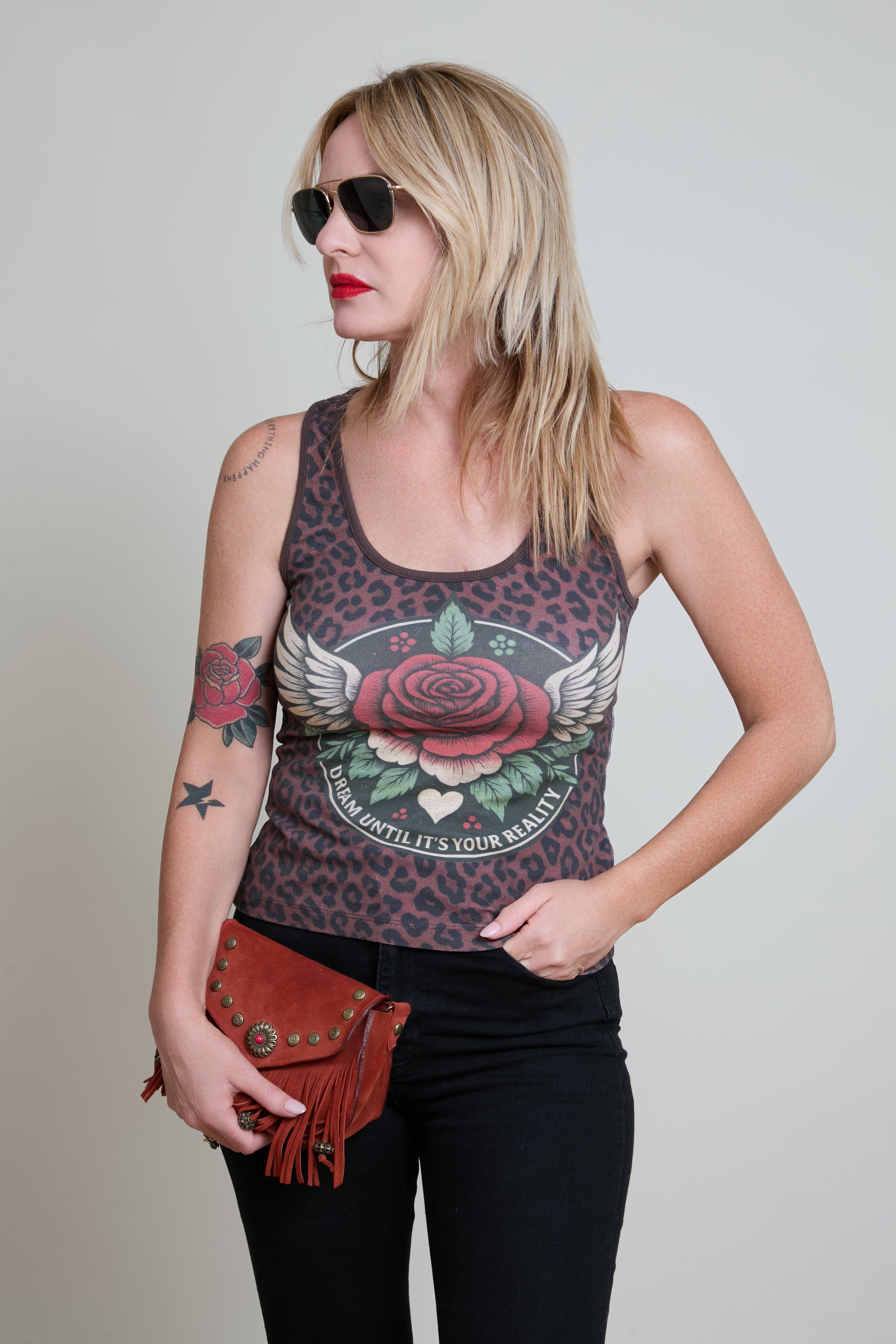 Woman wearing a tank top with a rose design and sunglasses, holding a red purse.