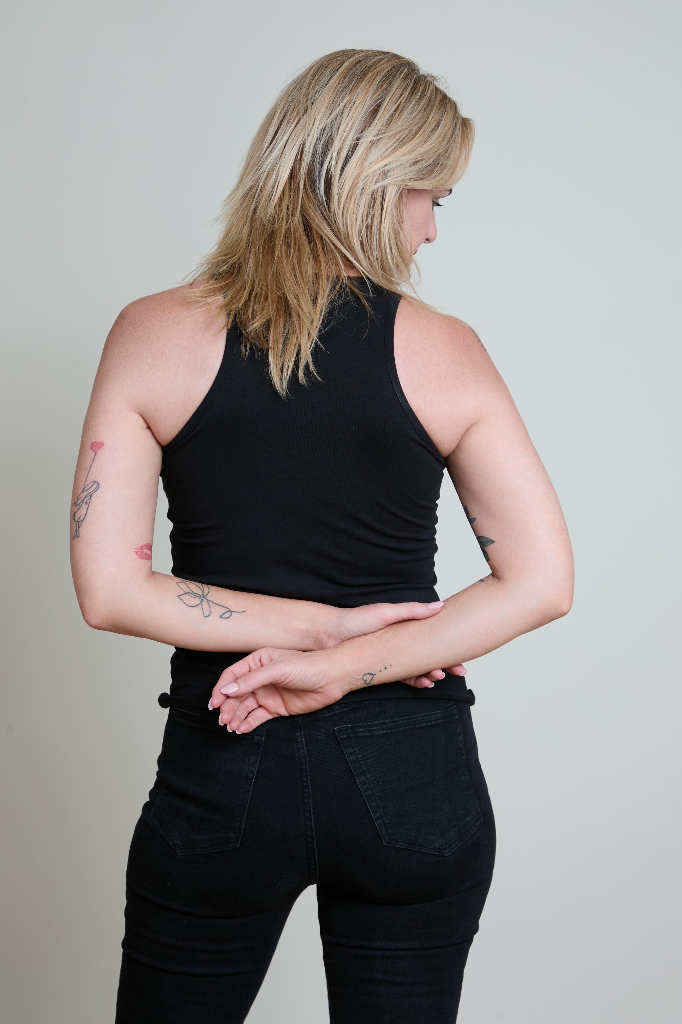 Person wearing a black tank top and black pants against a plain background