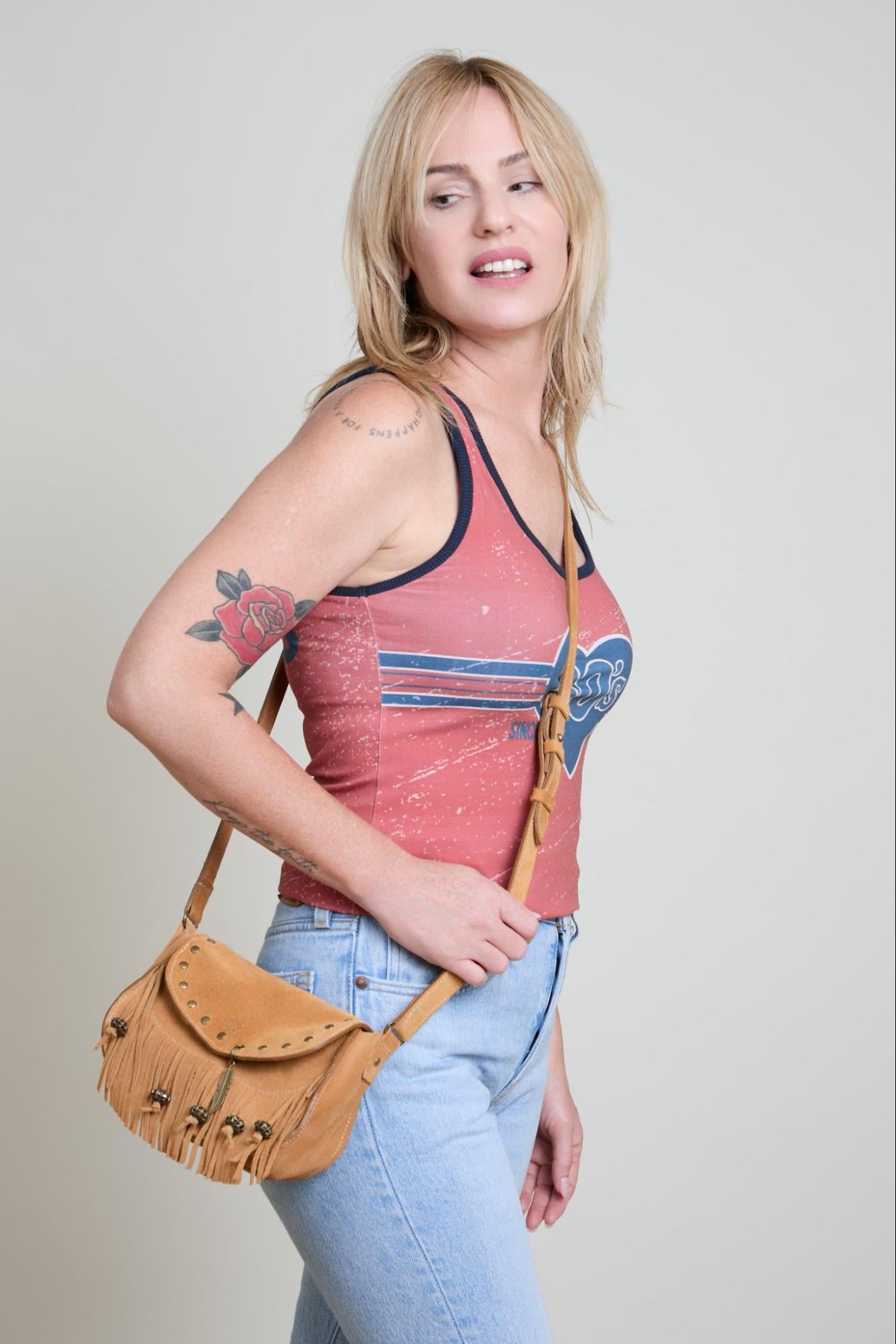 Woman wearing a red tank top with blue designs and holding a brown leather bag against a plain background