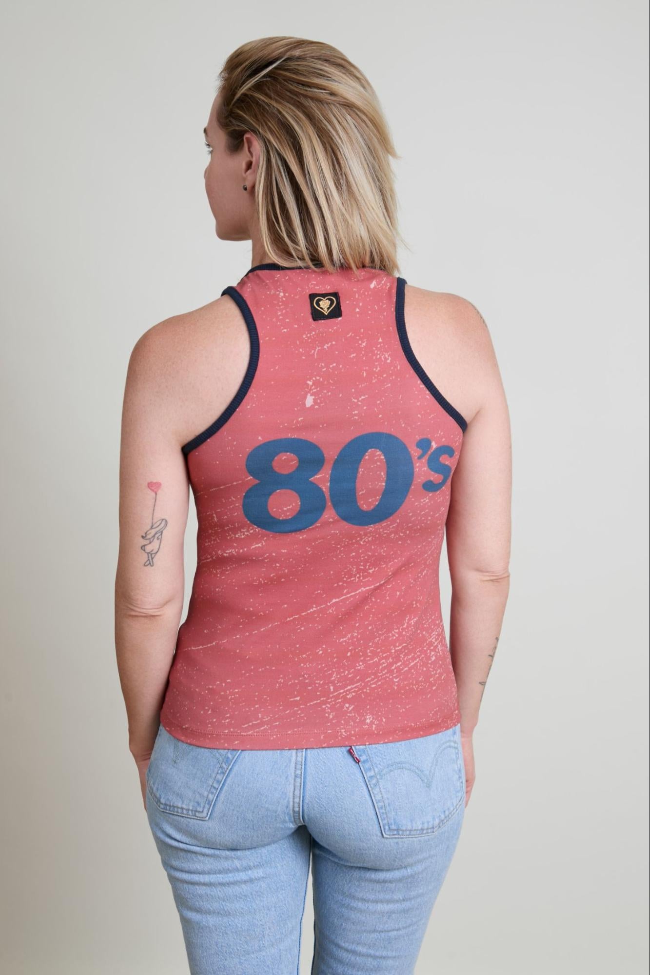 Person wearing a red tank top with '80s' printed on the back, standing against a plain background.