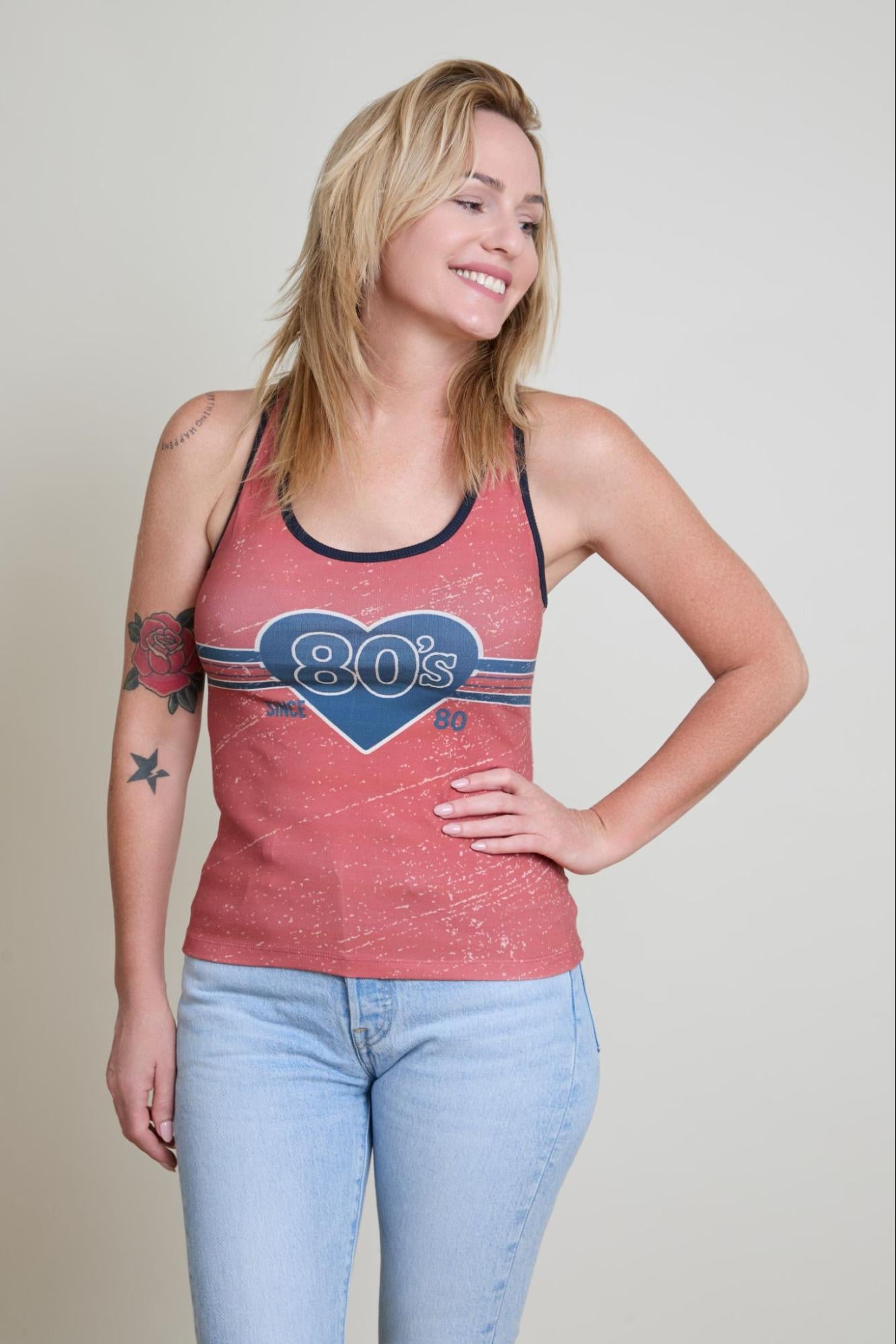 Woman wearing a red tank top with '80s' design and light blue jeans on a plain background