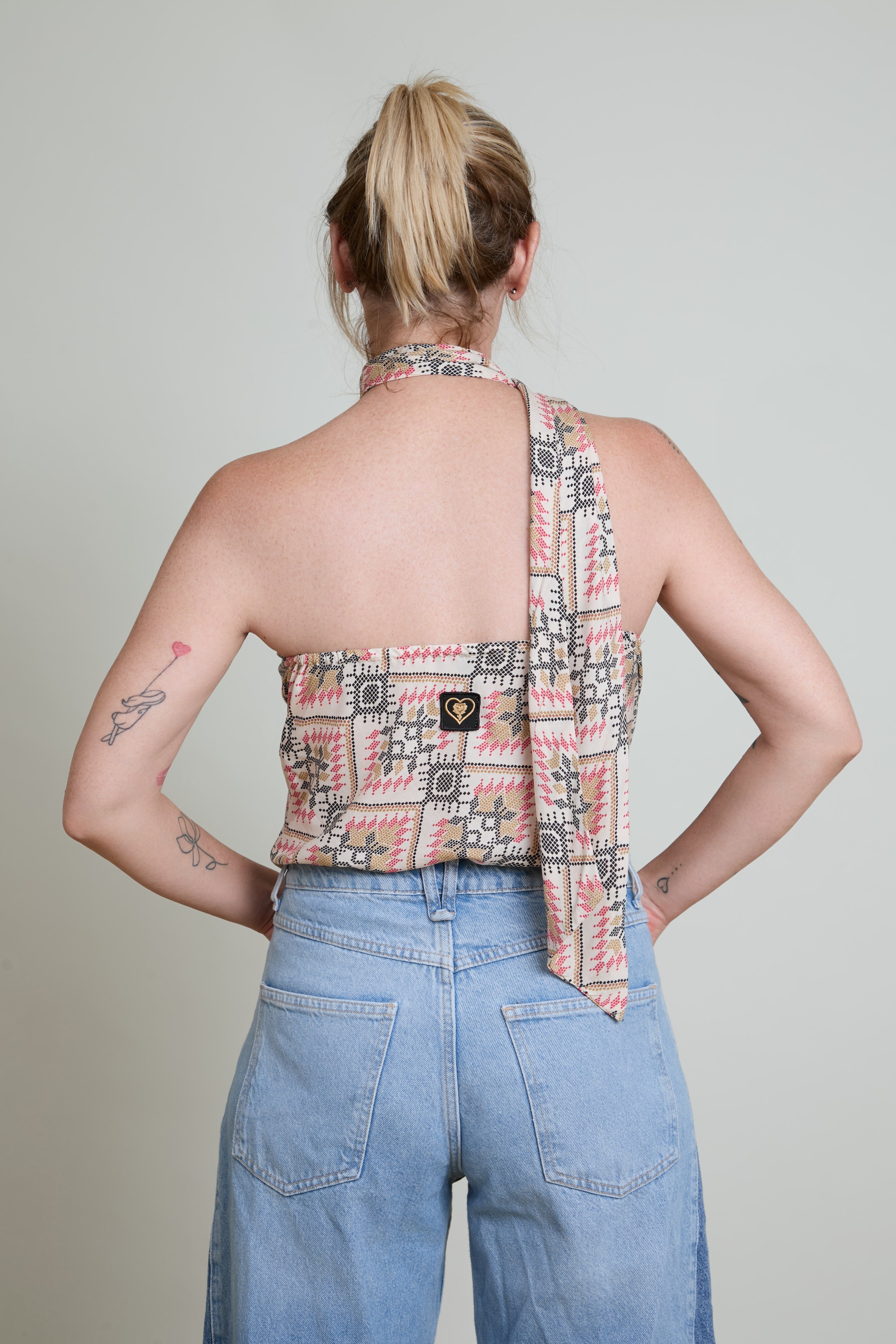 Person wearing a patterned halter top and blue jeans against a plain background