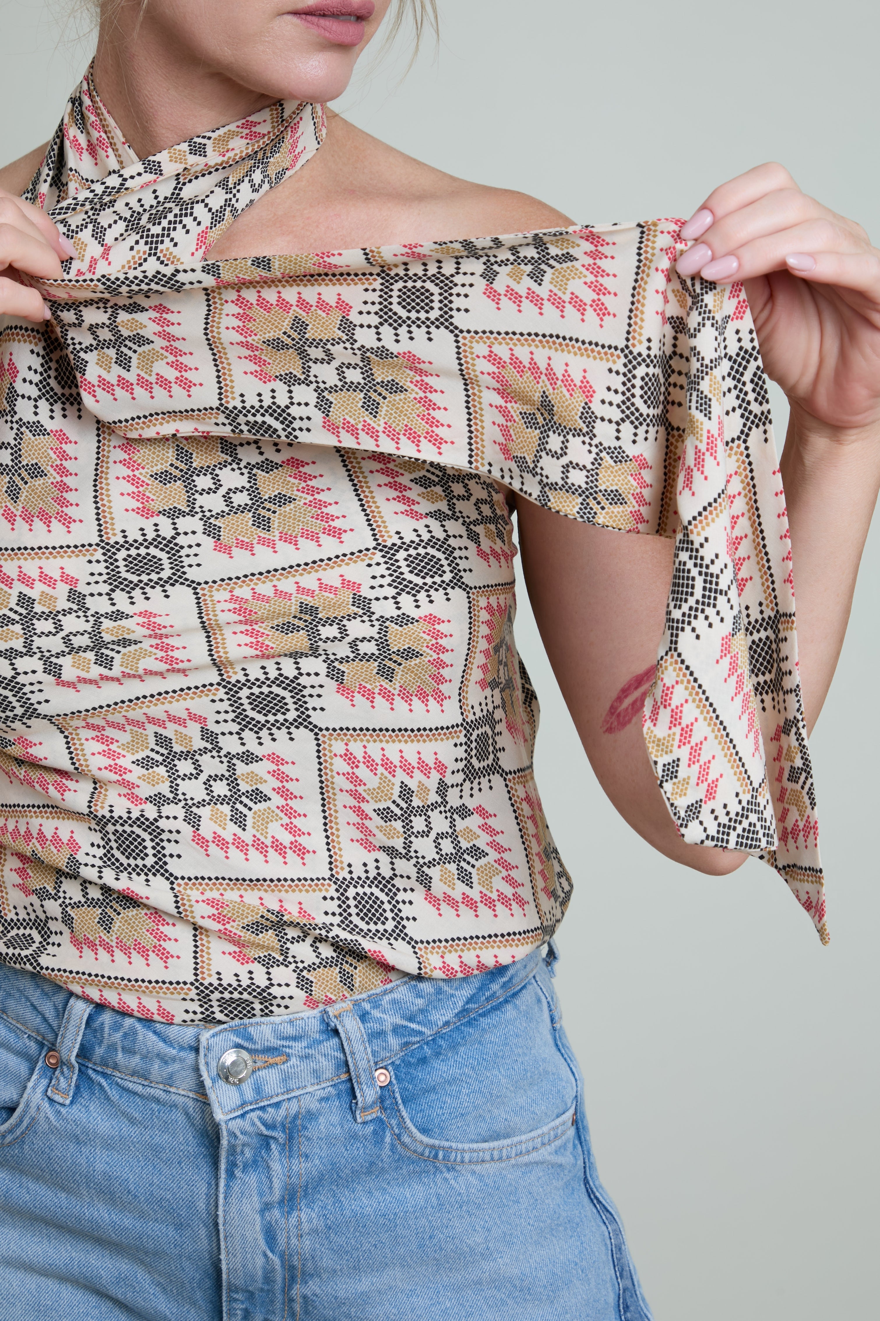 Person wearing a patterned top and blue jeans against a plain background