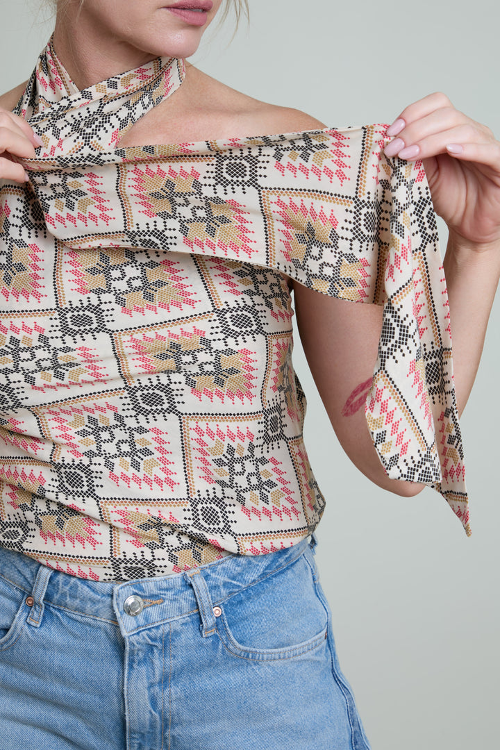 Person wearing a patterned top and blue jeans against a plain background