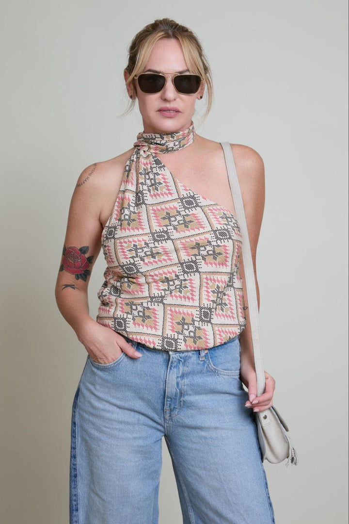 Woman wearing a patterned top and jeans with sunglasses on a plain background