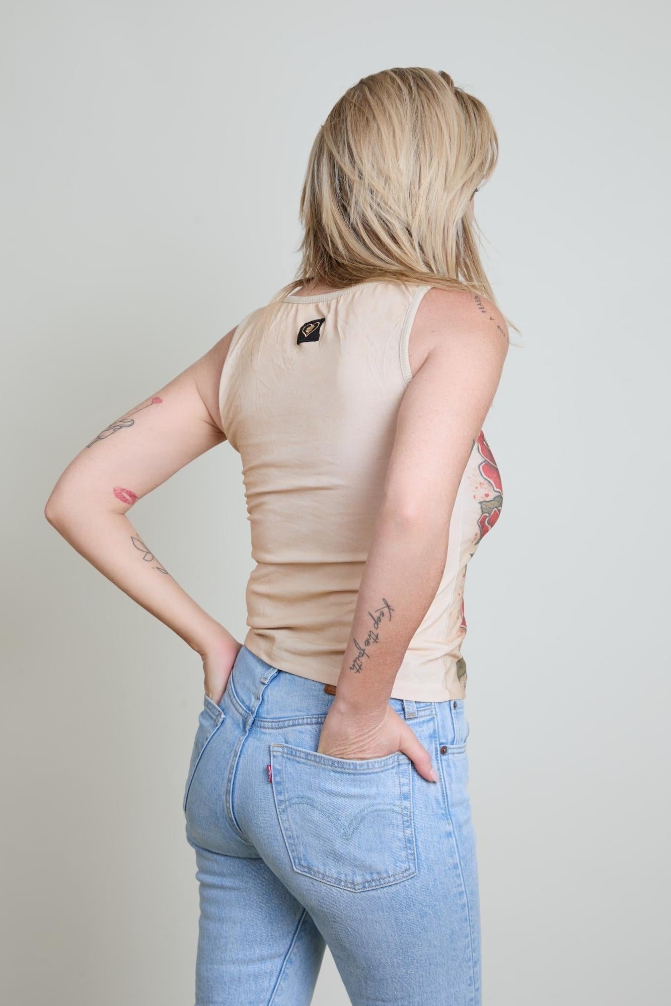 Person wearing a beige sleeveless top and blue jeans against a plain background