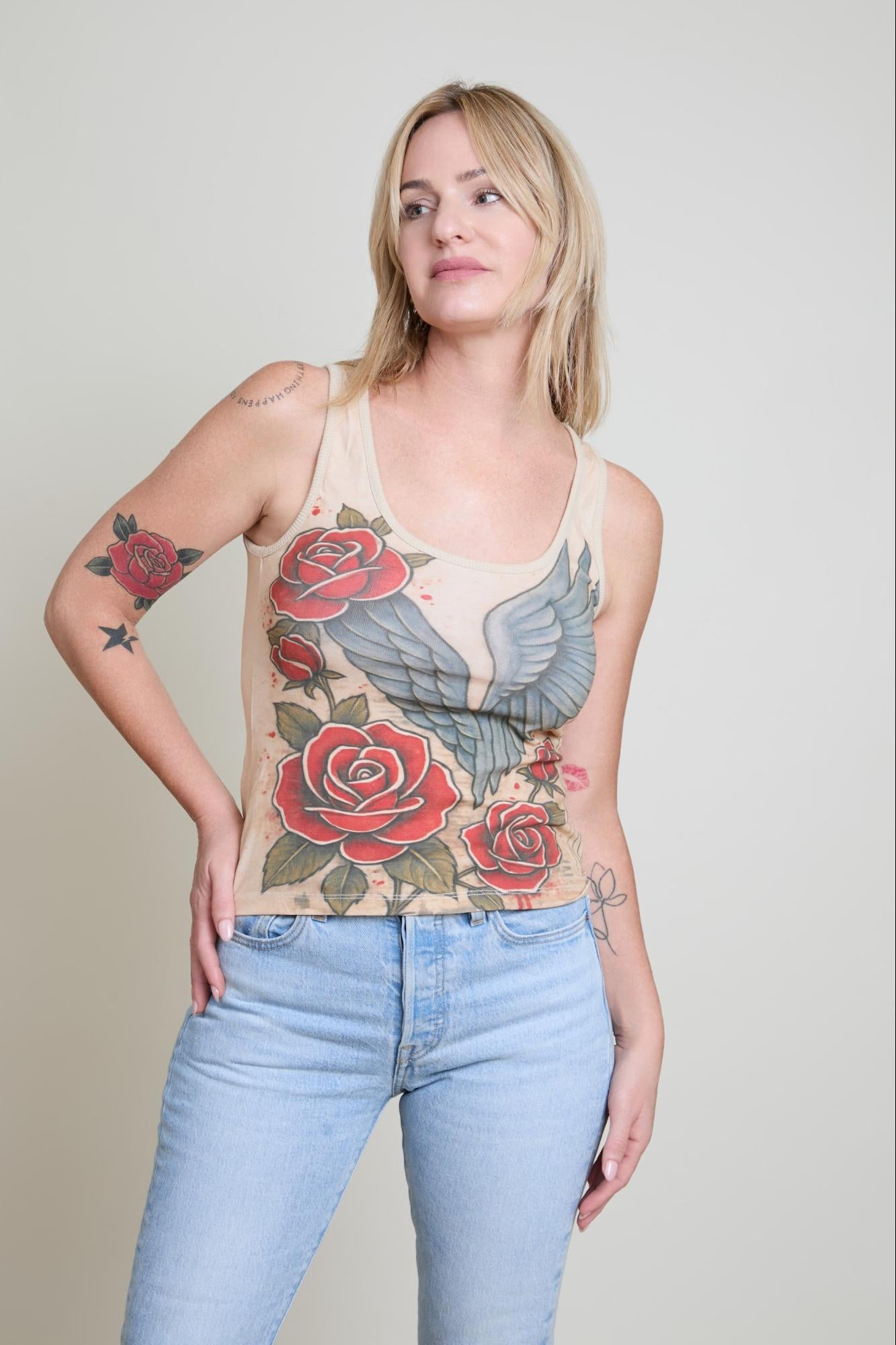 Woman wearing a tank top with floral and eagle design and light blue jeans.