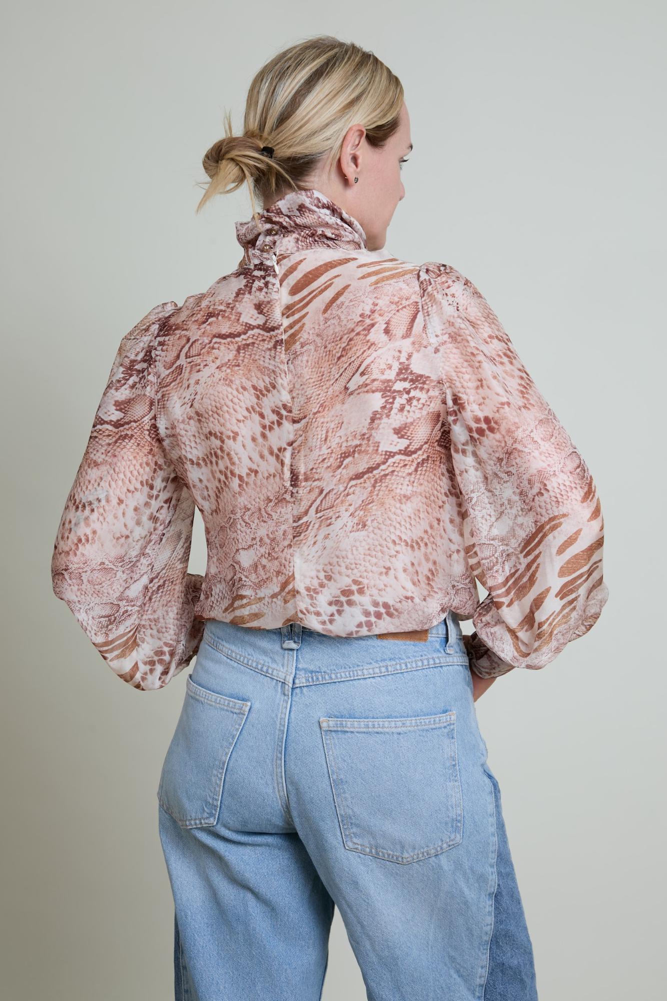 Person wearing a patterned blouse and blue jeans against a plain background