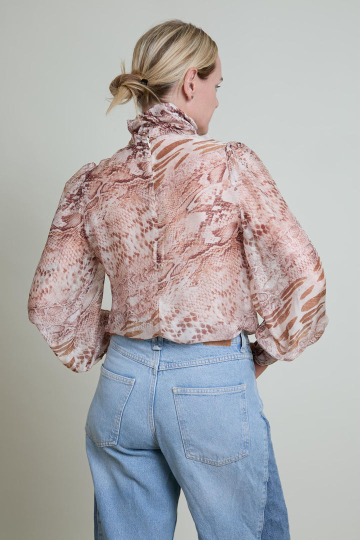 Person wearing a patterned blouse and blue jeans against a plain background