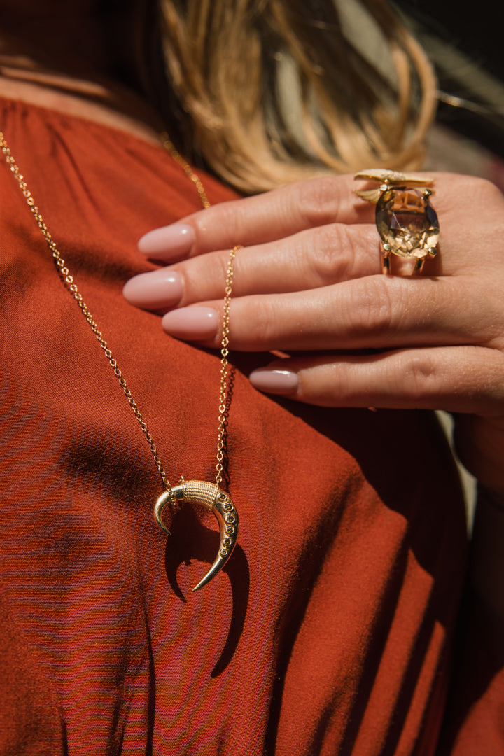 Gold necklace with a unique pendant worn by a person in a red garment.