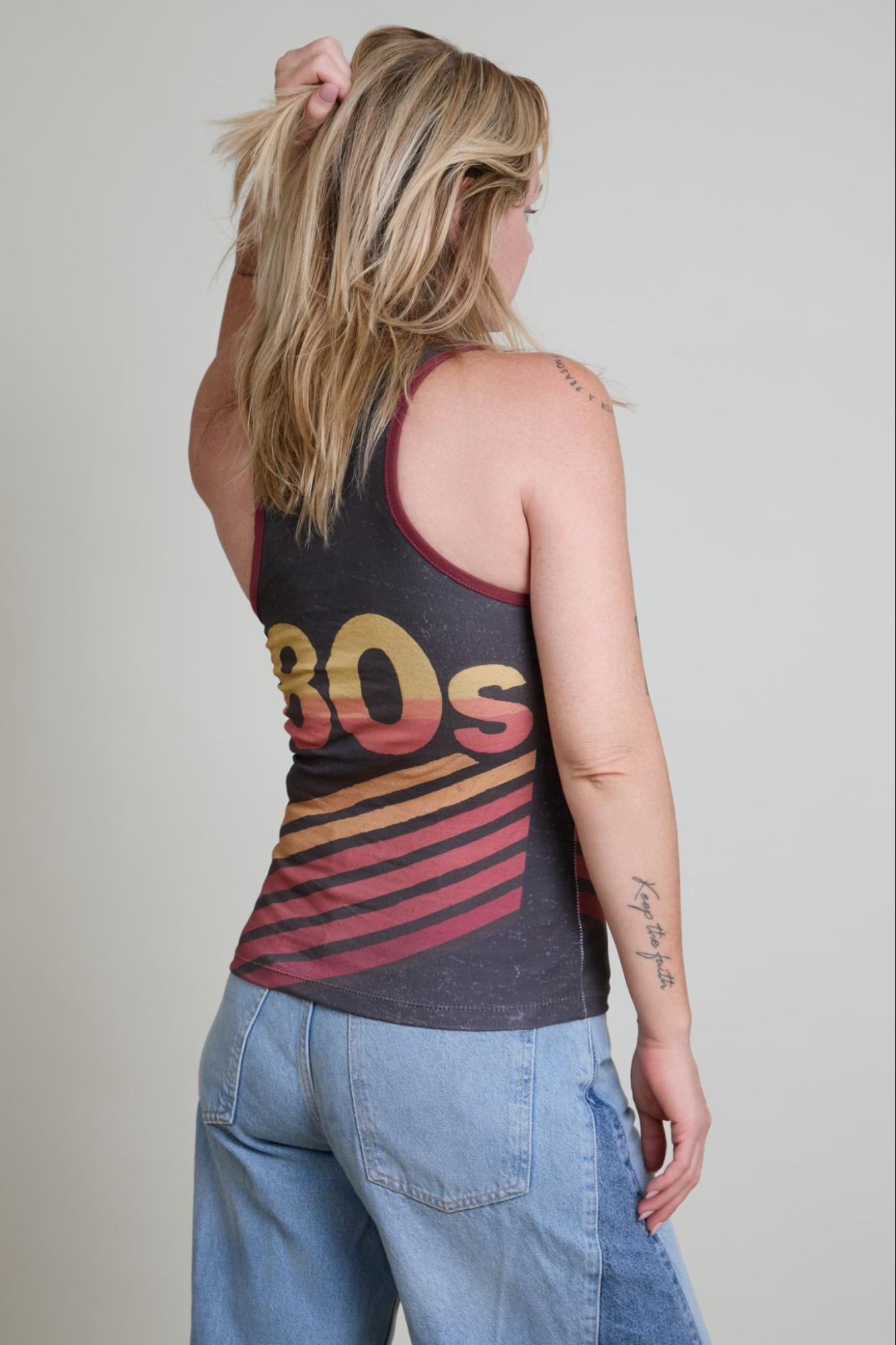 Person wearing a tank top with '80s' design and blue jeans on a plain background