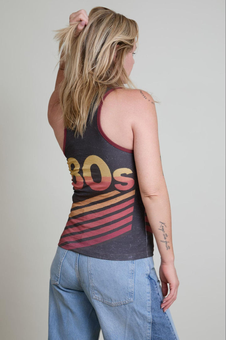 Person wearing a tank top with '80s' design and blue jeans on a plain background