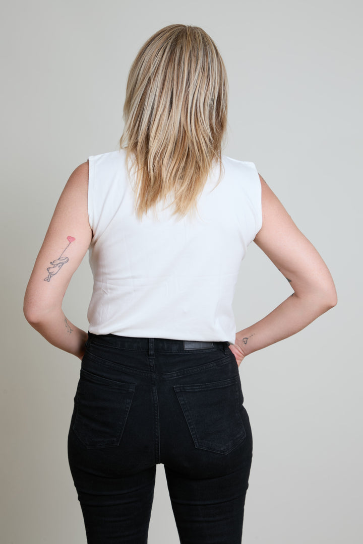 Person wearing a white sleeveless top and black pants against a plain background