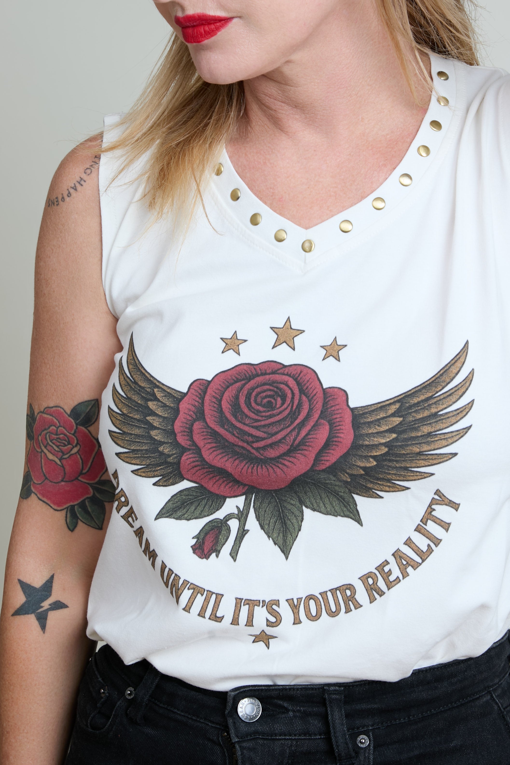 White sleeveless shirt with red rose and wings design and text, worn by a person.