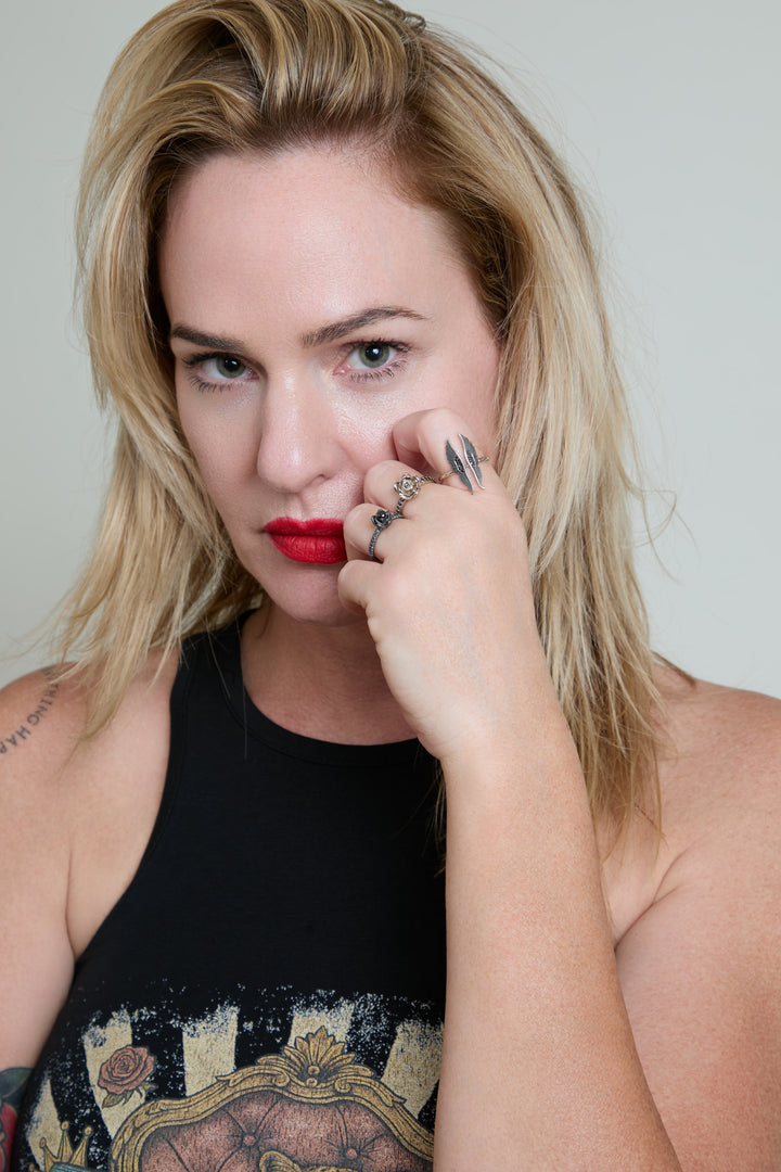 Woman with tattoos and red lipstick posing against a plain background