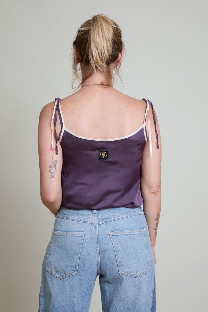 Person wearing a purple tank top and blue jeans against a plain background