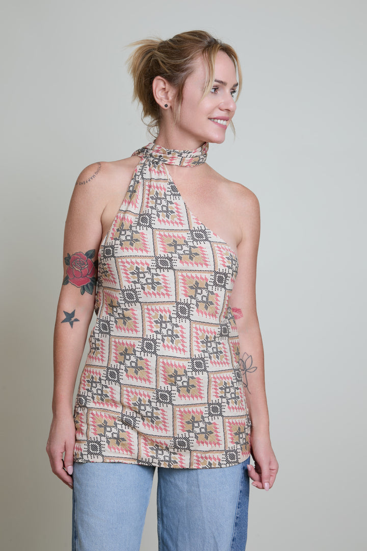 Woman wearing a patterned halter top and jeans against a plain background